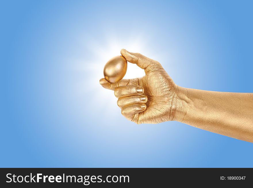 Gold egg in a gold man's hand against the blue sky