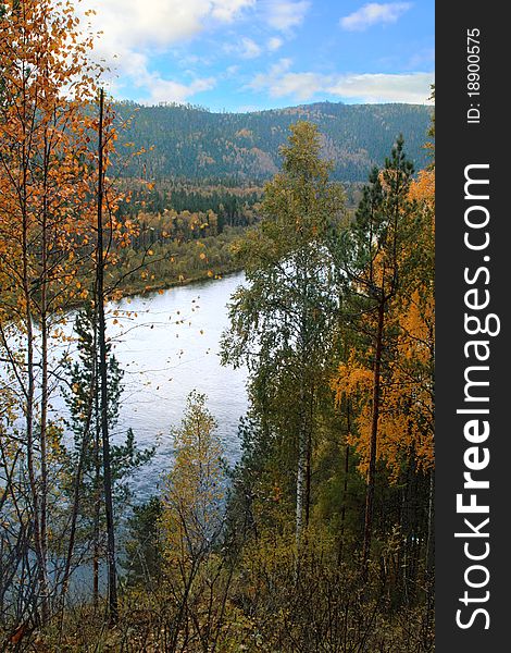 Autumn landscape with river, mountains and multi-colored forest.