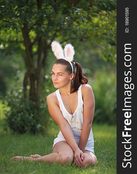 Woman with funny rabbit ears sits on a grass outdoors