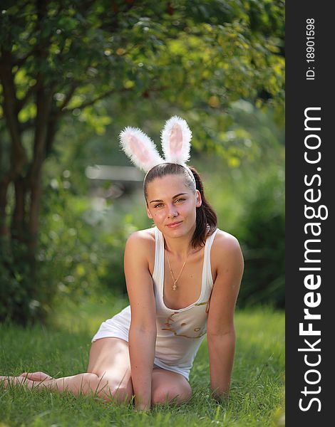 Woman with funny rabbit ears sits on a grass outdoors