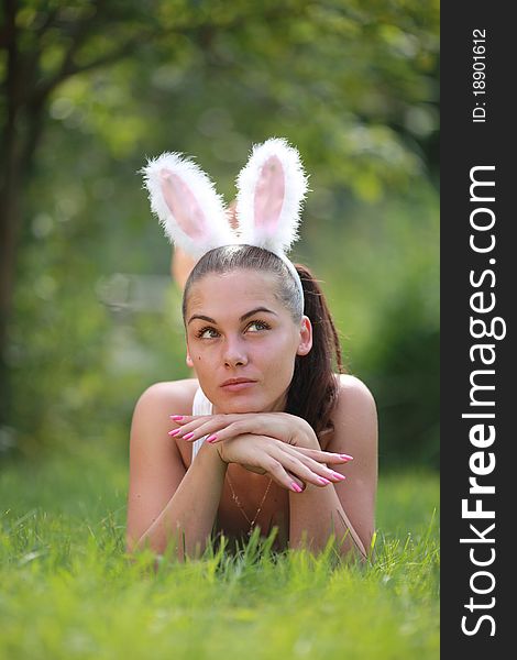 Woman with funny rabbit ears lies on a grass outdoors