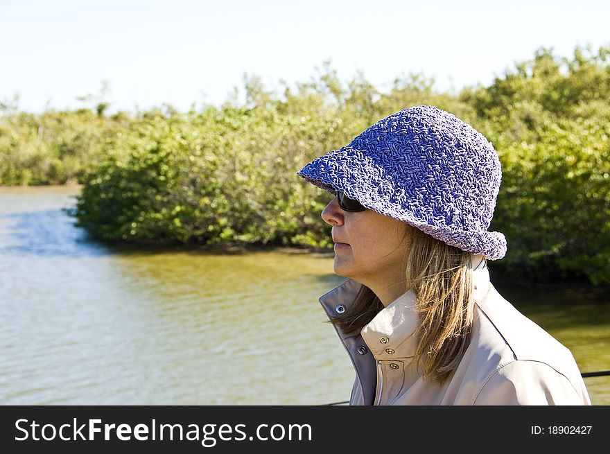 Profile of a woman in hat & sunglasses overlooking a river winding through a forest. Profile of a woman in hat & sunglasses overlooking a river winding through a forest.