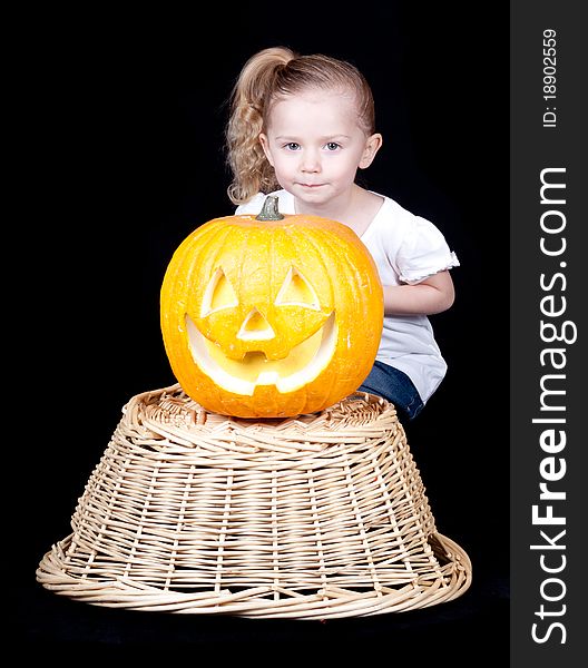 A pumpkin on a harvest basket with a child kneeling behind. A pumpkin on a harvest basket with a child kneeling behind.