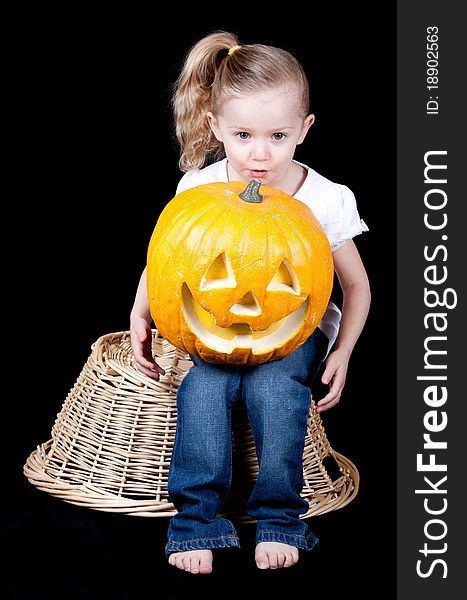 An adorable girl holding a pumpkin on her lap. She is itting on a harvest basket. An adorable girl holding a pumpkin on her lap. She is itting on a harvest basket.