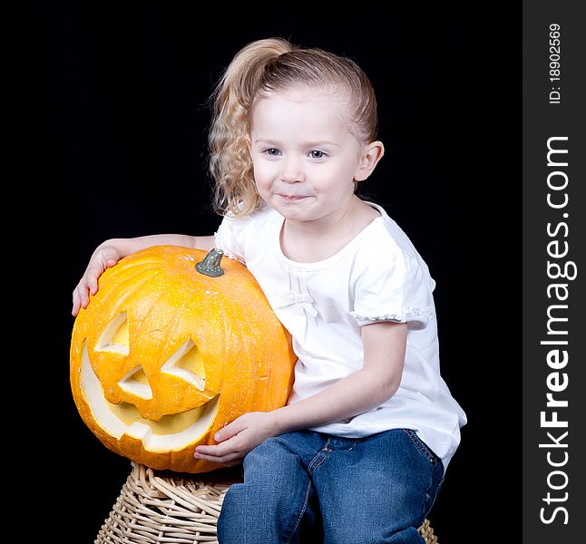 A girl is sitting on a harvest basket holding her pumpkin. A girl is sitting on a harvest basket holding her pumpkin.