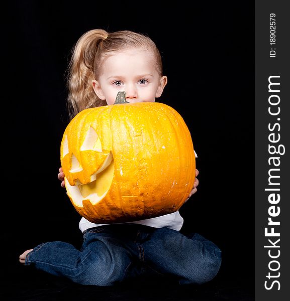 A young child is holding a pumpkin. The pumpkin is sideways and the child is kneeling. A young child is holding a pumpkin. The pumpkin is sideways and the child is kneeling.