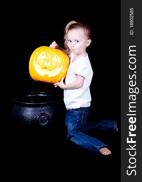 A young girl is trying to make pumpkin pie with a pumpkin and a witches cauldron.