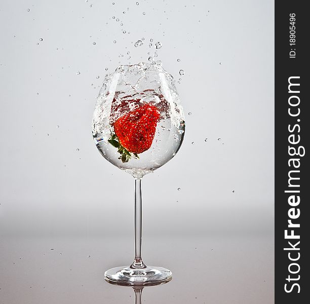 One red strawberry fallen into a glass of water. One red strawberry fallen into a glass of water