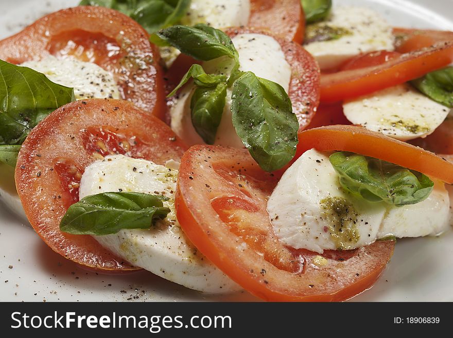 Plate of fresh mozzarella cheese, slices of ripe tomatoes and fresh basil leaves with sprinkle of three color peppercorns. Plate of fresh mozzarella cheese, slices of ripe tomatoes and fresh basil leaves with sprinkle of three color peppercorns