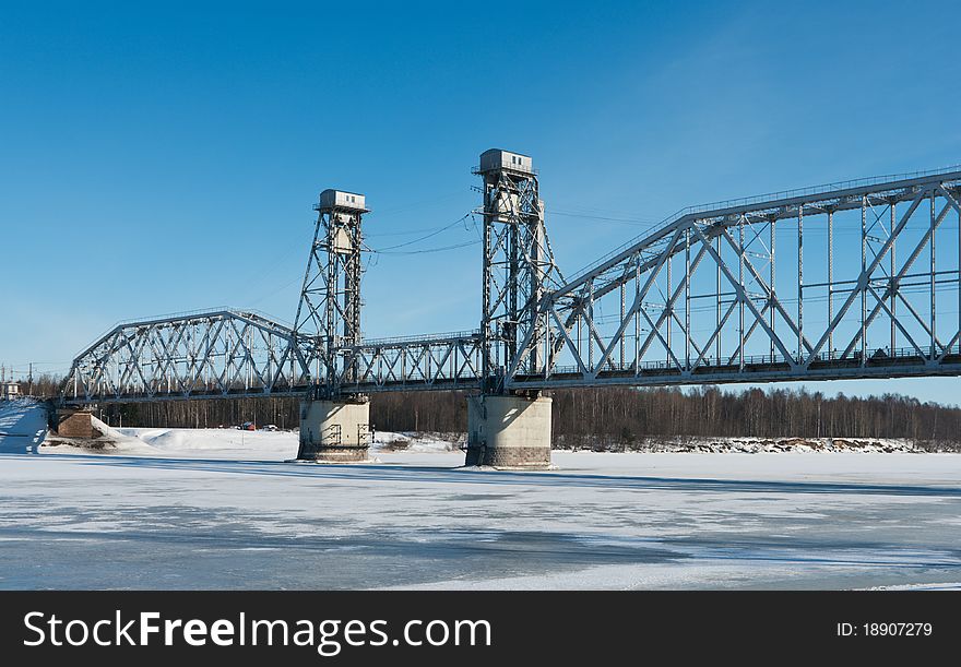 Railroad bridge across the frozen river on the background of blue sky