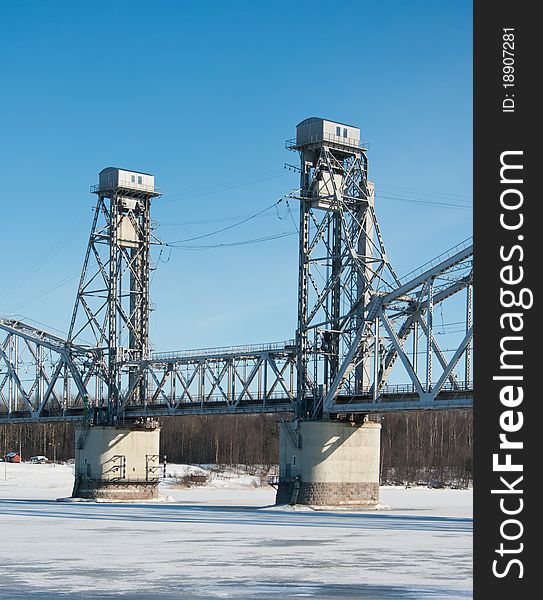 Railroad bridge across the frozen river on the background of blue sky