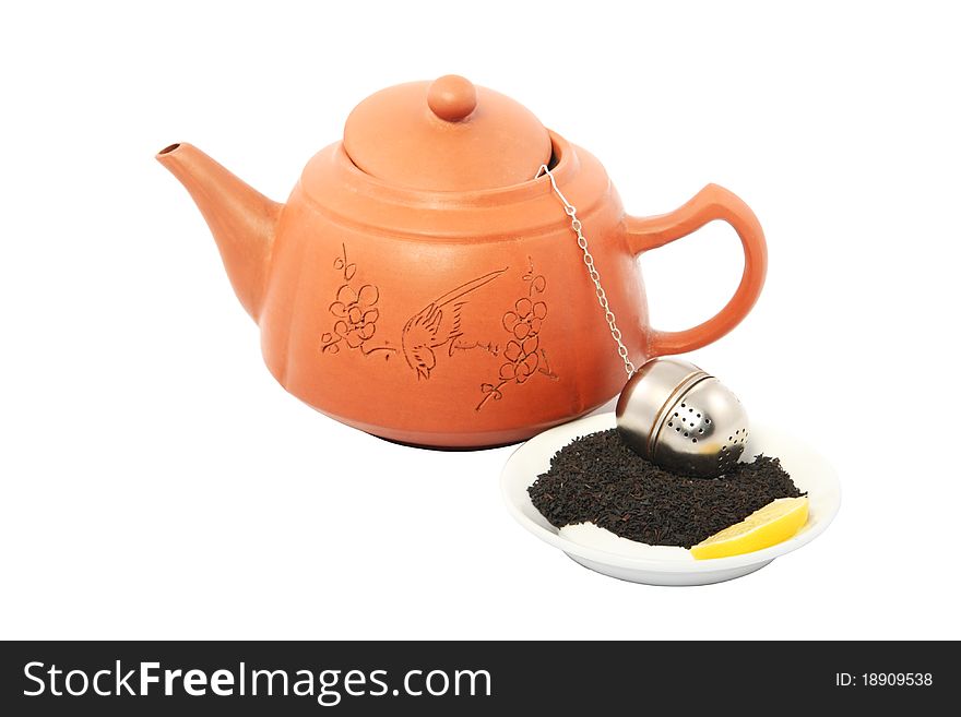 Clay red teapot with a strainer, tea leaves and a lemon on a white saucer on the isolated white background. Clay red teapot with a strainer, tea leaves and a lemon on a white saucer on the isolated white background