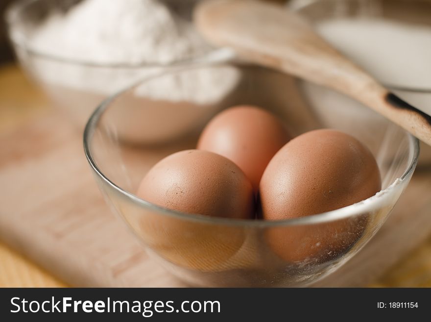 Close up of three eggs on a bowl, and a bowl with flour out of focus on background. Close up of three eggs on a bowl, and a bowl with flour out of focus on background