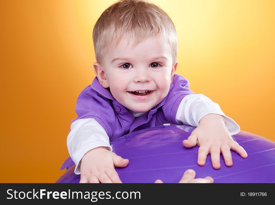 Happy little boy laughs near violet ball looking at camera