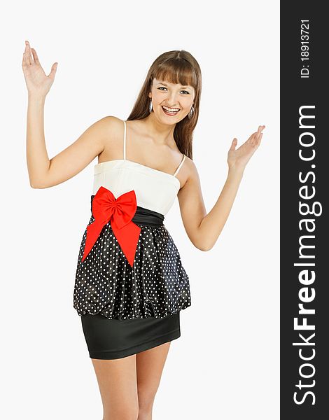 Beautiful fashion girl rejoices with her hands up. A look at the camera. Black skirt with white polka dots. Topic white with a red bow at the waist. On a white background.