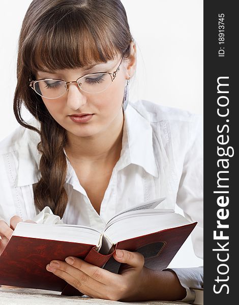 Beautiful girl with glasses in a white shirt thoughtfully reading a book. Her Hair is braided into a braid. Focus on the forefront of the book. Close-up. Photographed in a studio against a white background. Beautiful girl with glasses in a white shirt thoughtfully reading a book. Her Hair is braided into a braid. Focus on the forefront of the book. Close-up. Photographed in a studio against a white background.