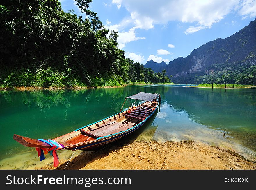 Boat on the shore of lake in Thailand with mountain as background