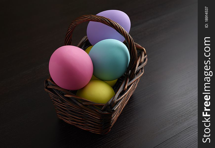 Large, colorful Easter eggs in brown basket. Copy space to right or left of basket