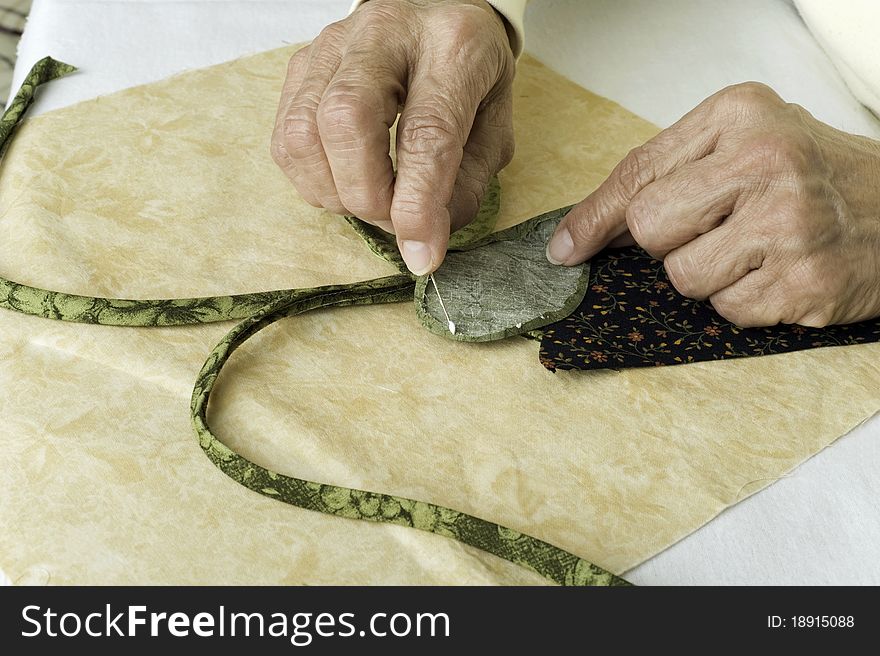 A quilter applies fabric glue to a leaf made of fabric for applique to background foundation. A quilter applies fabric glue to a leaf made of fabric for applique to background foundation.