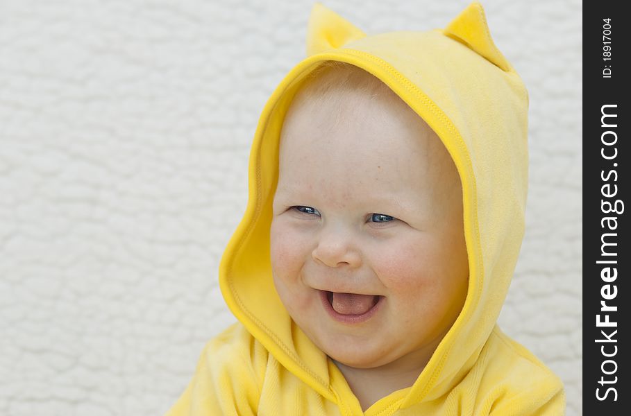 Portrait of the little girl (6 months) in a yellow hood which smiles on a light background. Portrait of the little girl (6 months) in a yellow hood which smiles on a light background