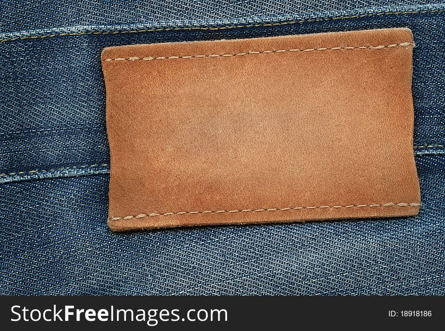 Blank leather jeans label sewed on a blue jeans. Can be used as background for your text.