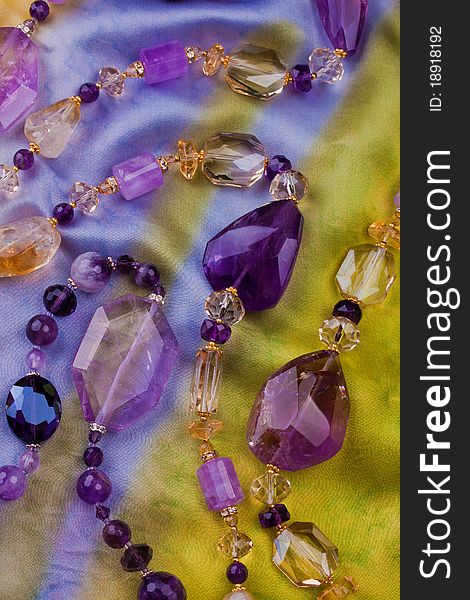 Beautiful necklace of big violet and yellow amethysts laid on bright multicolored silk cloth. Beautiful necklace of big violet and yellow amethysts laid on bright multicolored silk cloth