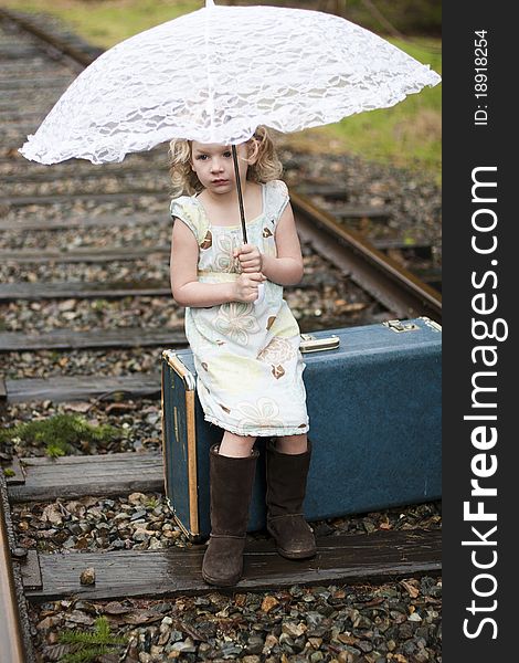 Young girl sitting on her suitcase holding her umbrella waiting for the train. Young girl sitting on her suitcase holding her umbrella waiting for the train