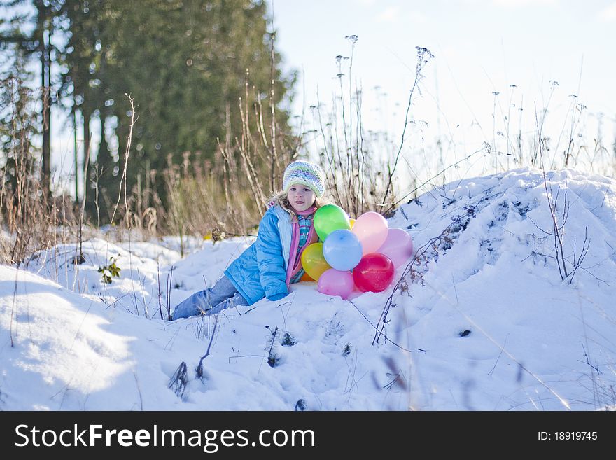 Happy young gril in the middle of a field holding balloons in the snow