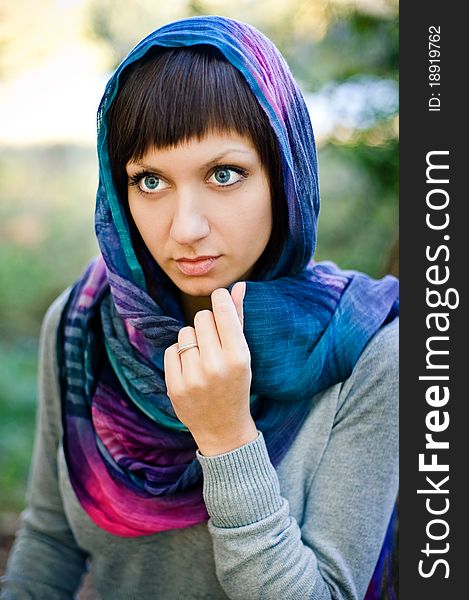 The girl in a scarf and in a knitted dress sits on a tree.