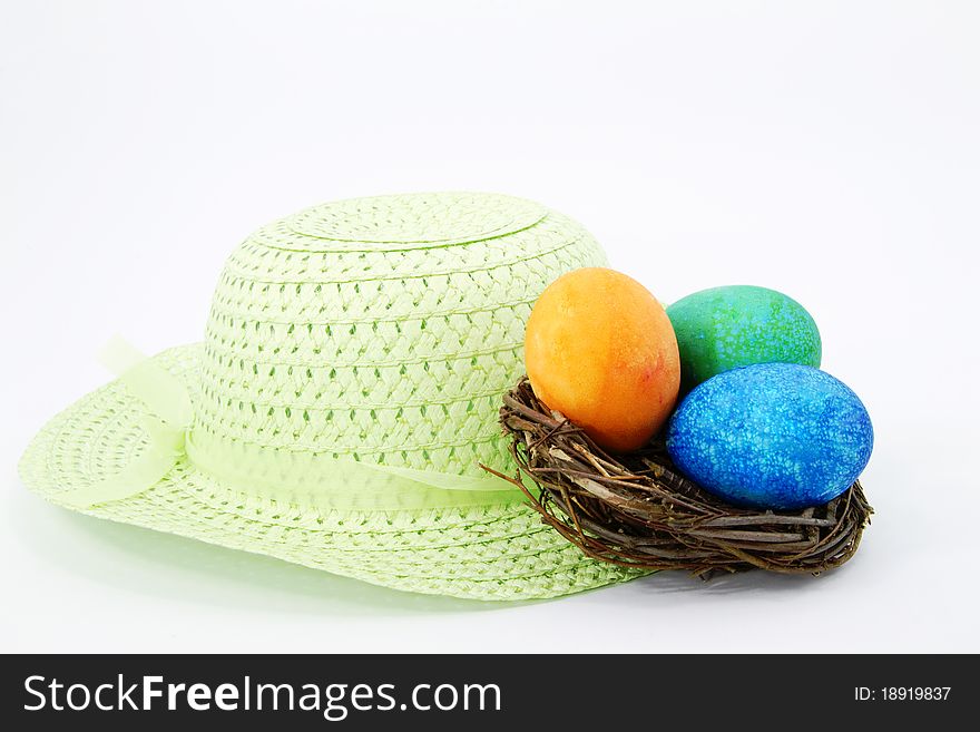 Spring green Easter bonnet with light green ribbon sits with Easter eggs dyed orange, green, and blue. Spring green Easter bonnet with light green ribbon sits with Easter eggs dyed orange, green, and blue