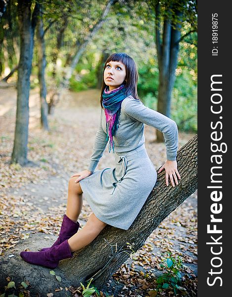 The girl in a scarf and in a knitted dress sits on a tree.
