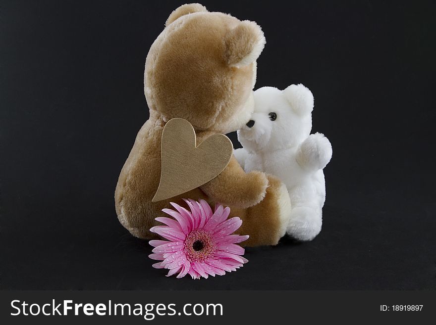 Tan stuffed bear, gold heart on her shoulder and pink flower by her side, kisses smaller stuffed bear. Tan stuffed bear, gold heart on her shoulder and pink flower by her side, kisses smaller stuffed bear