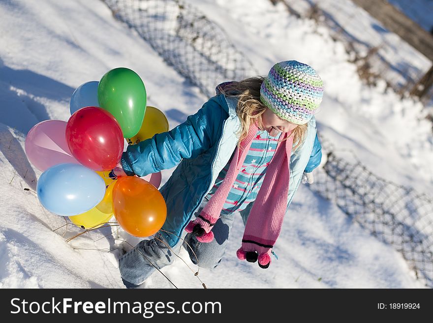 Young girl in a field of snow playing around with some balloons.