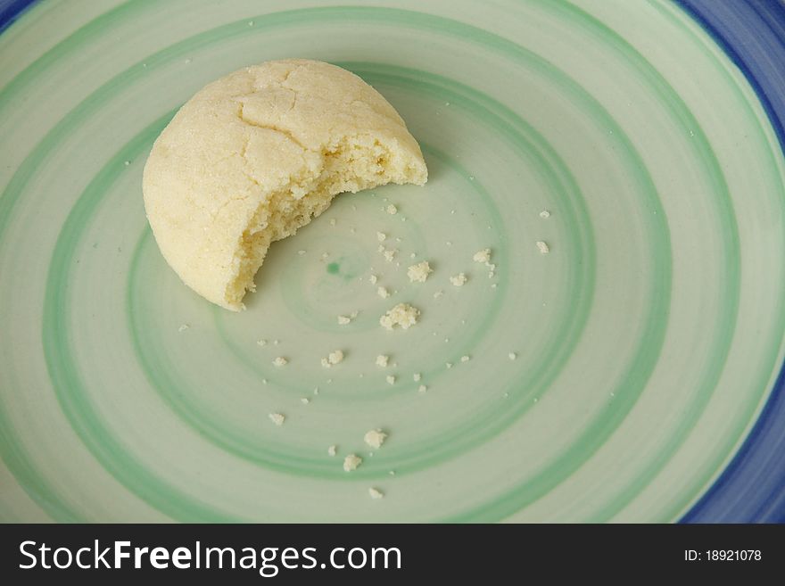 A cookie with a bite out of it lying on a plate with crumbs. A cookie with a bite out of it lying on a plate with crumbs