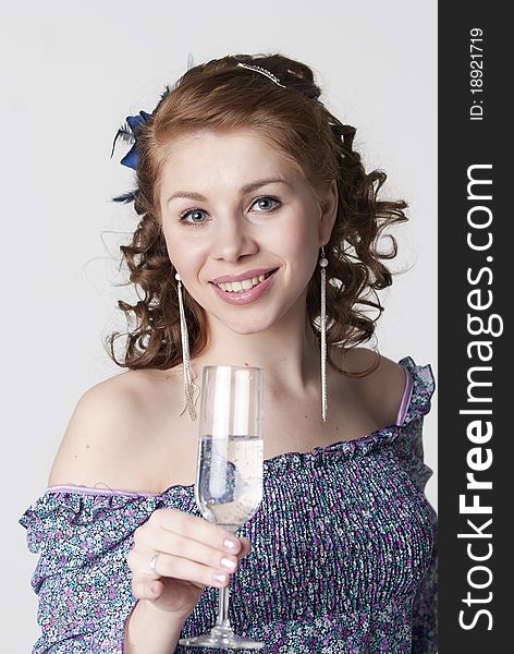 The young beautiful girl has control over a glass of water and smiles on a light background
