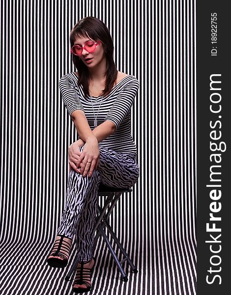 Cute girl in a striped clothes and pink sunglasses on the striped background