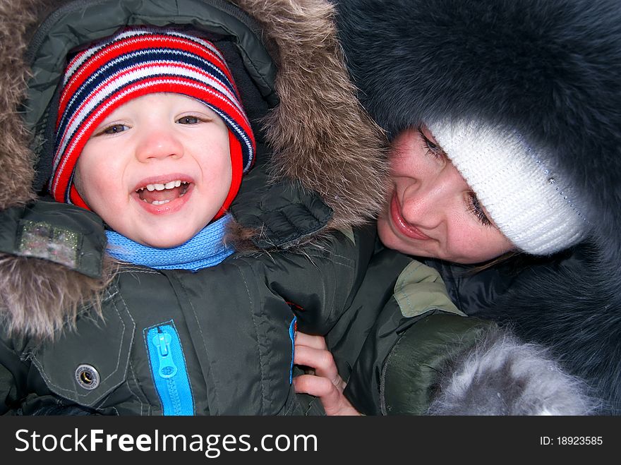 In the winter mother holds on hands of the laughing child in winter clothes. In the winter mother holds on hands of the laughing child in winter clothes