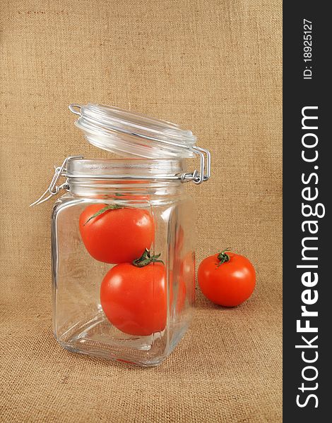 Red tomatoes in jar on jute background