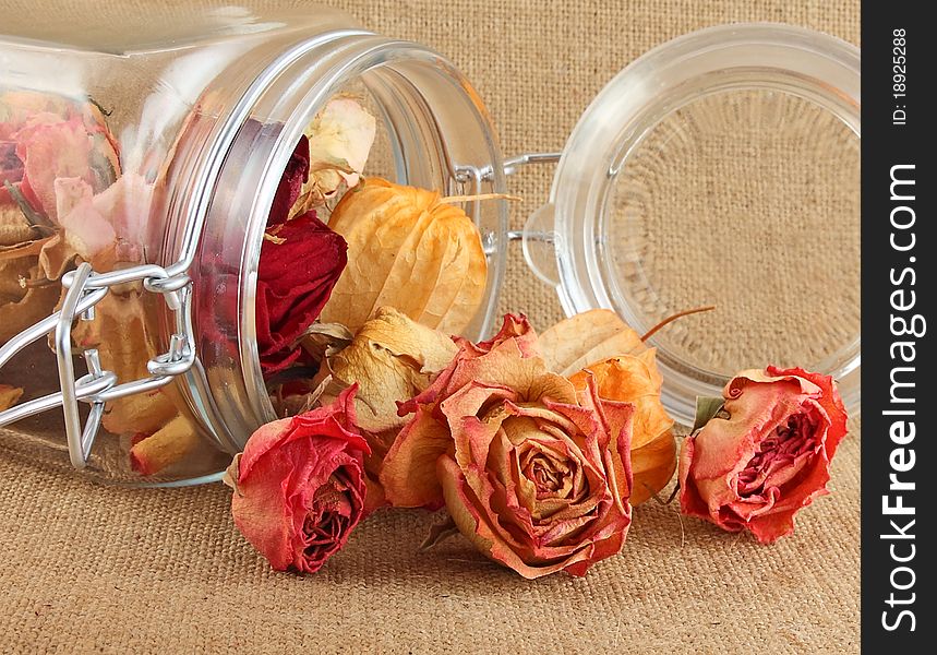 Buds of dry roses in glass bottle on jute background