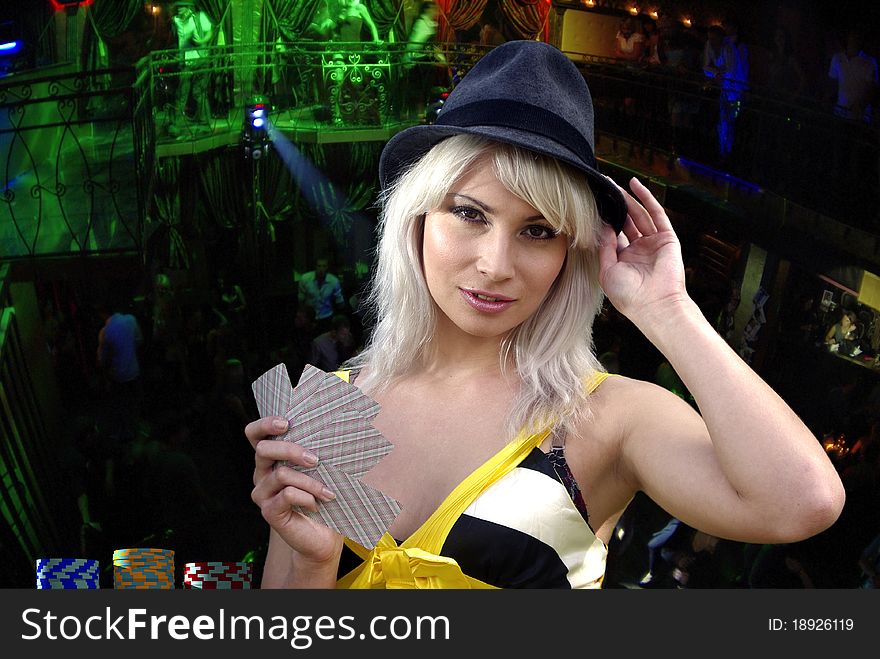 Blonde touching hat with cards in a hand looking intriguingly. Blonde touching hat with cards in a hand looking intriguingly