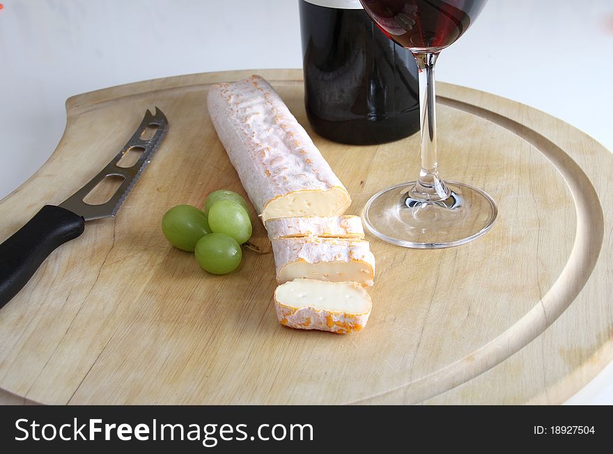 On the table sliced cheese and some green grapes and wine