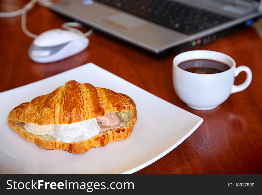 Hot coffee and croissant with ice-cream on office table with the laptop. Hot coffee and croissant with ice-cream on office table with the laptop