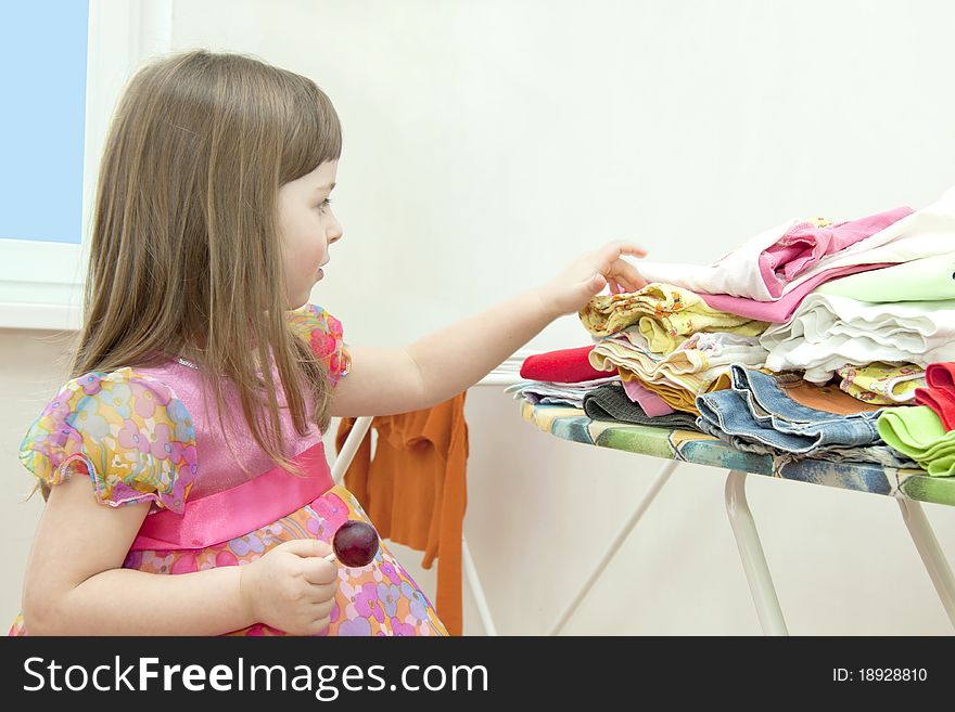 The girl in a beautiful dress costs near an ironing table and chooses things. The girl in a beautiful dress costs near an ironing table and chooses things