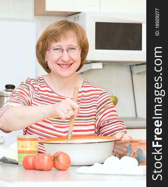 Joyful woman making dough in the kitchen at home