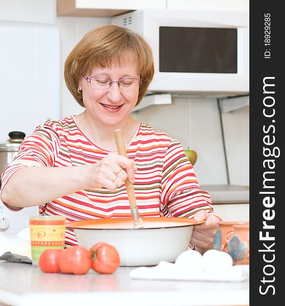 Joyful elderly woman cooking in the kitchen at home. Joyful elderly woman cooking in the kitchen at home