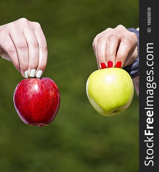 Two different hands holding two different apples in green background. Two different hands holding two different apples in green background