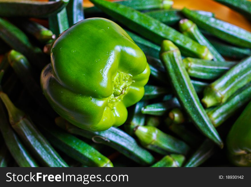 An arrangement of a ripe, green capsicum over plenty of ladies fingers. An arrangement of a ripe, green capsicum over plenty of ladies fingers.