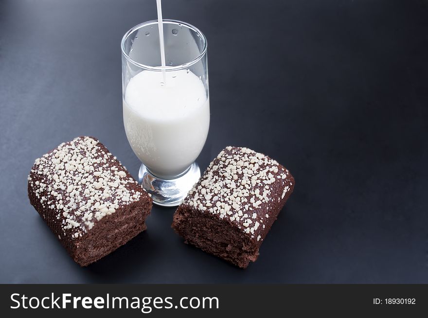 Chocolate roll and a glass of milk on a black background