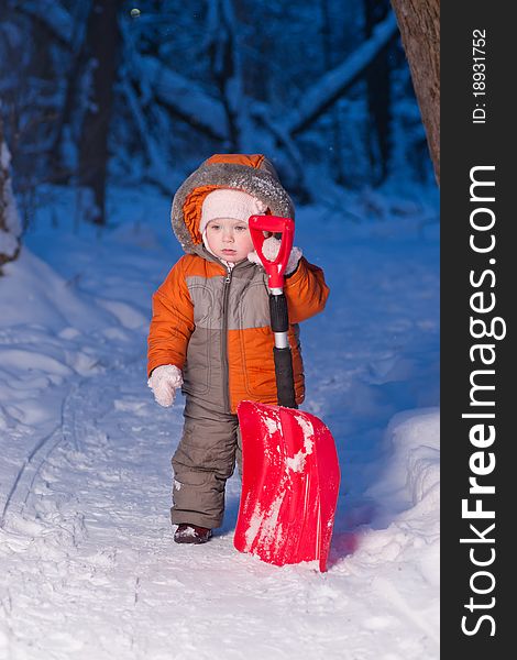 Portrait of adorable baby holding snow shovel and stay on road in park