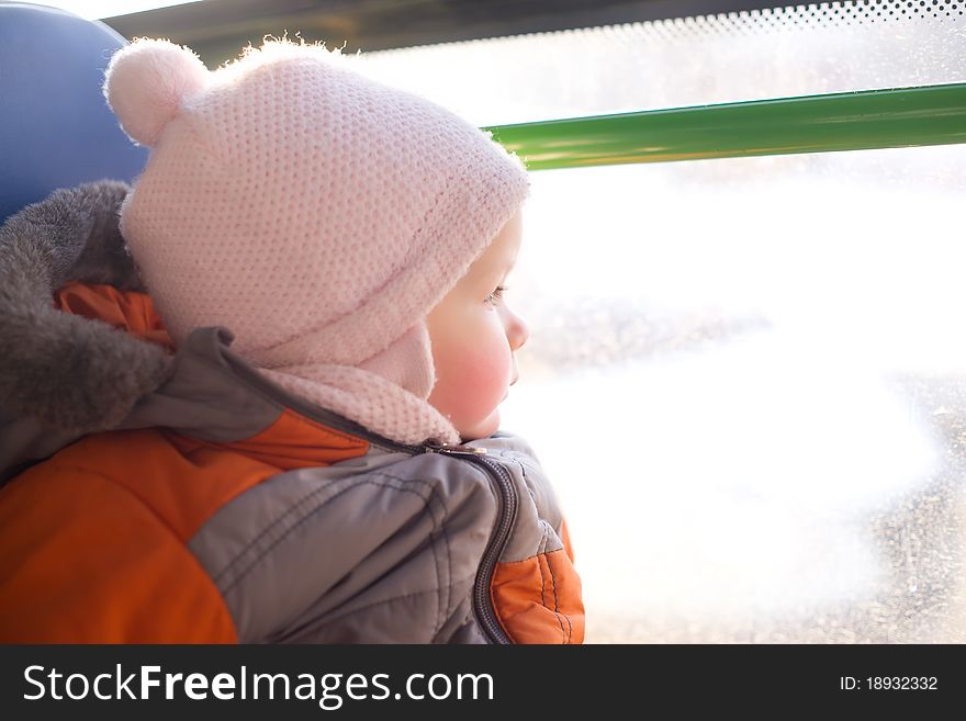 Adorable baby riding in city bus on seat place. Looking to window